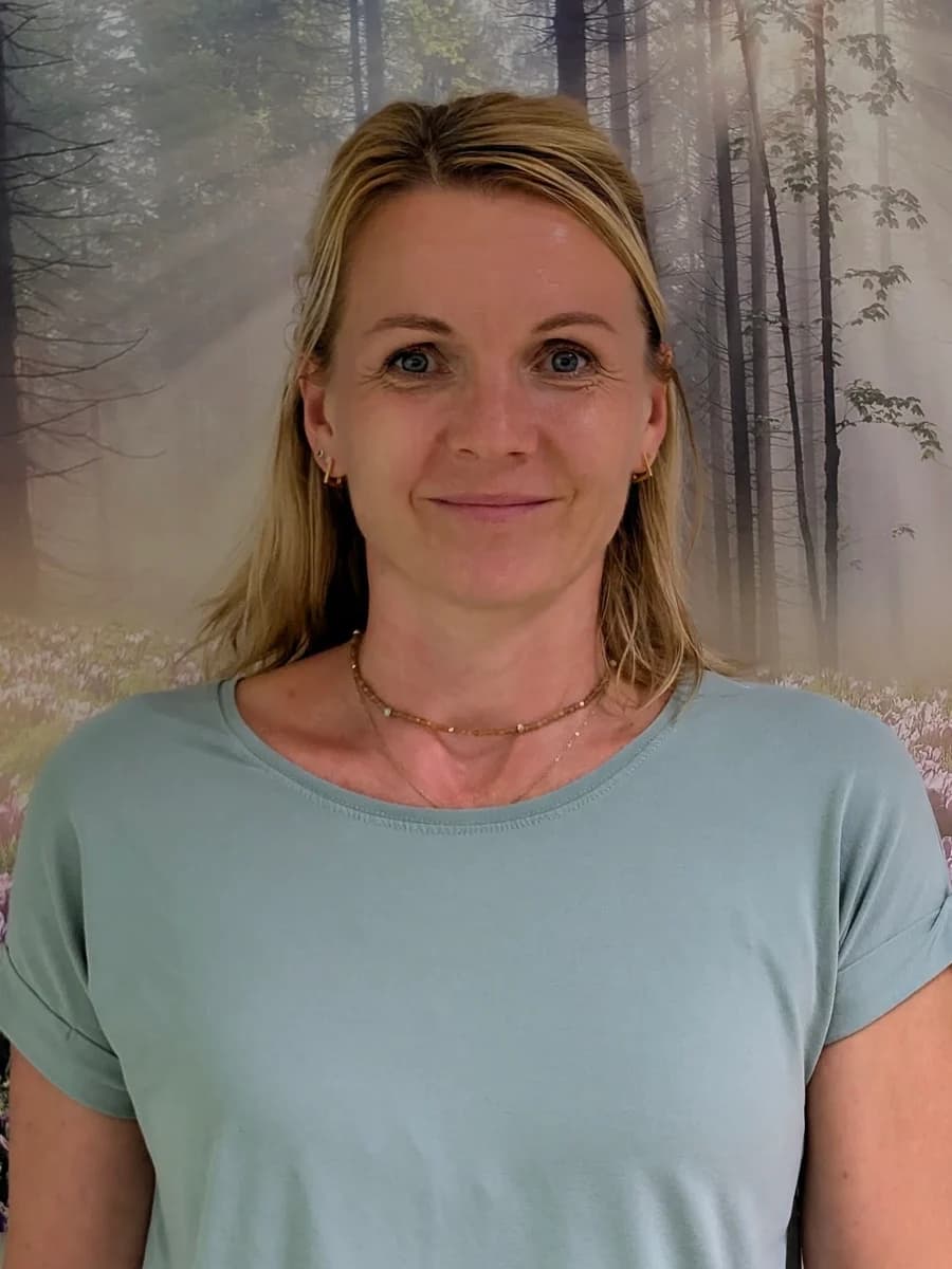 Claudia Lucke, Heilpraktikerin, vor der Waldtapete ihres Beratungsraums: schulterlanges blondes Haar, hellgrünes Shirt, den Blick in die Kamera gerichtet