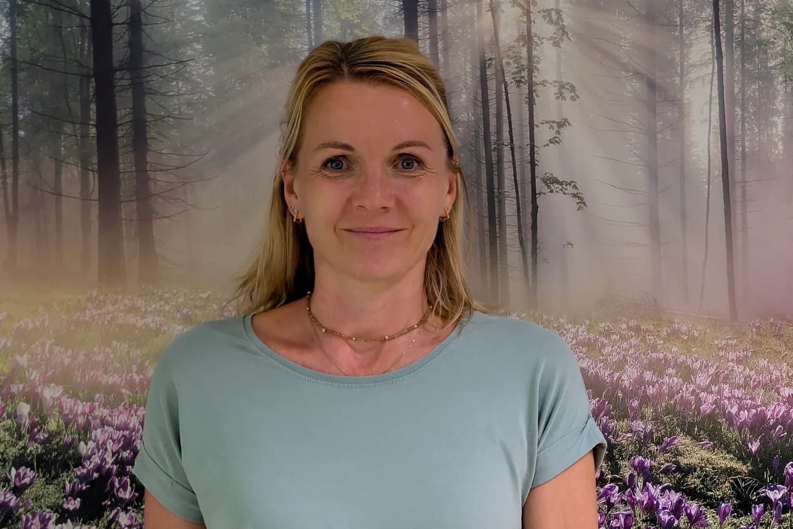 Claudia Lucke vor der Waldtapete ihres Beratungsraums, die eine neblige Kiefernlichtung über einer blühenden Krokuswiese zeigt